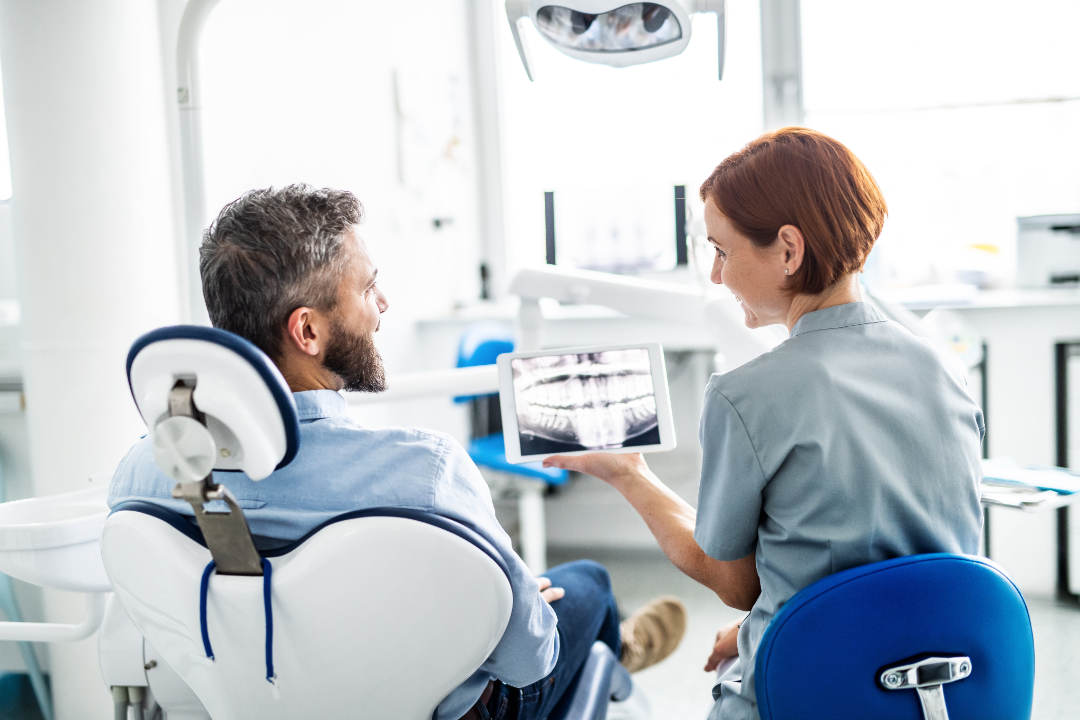 Dentist showing a male patient a dental X-ray on a tablet in a bright dental office.