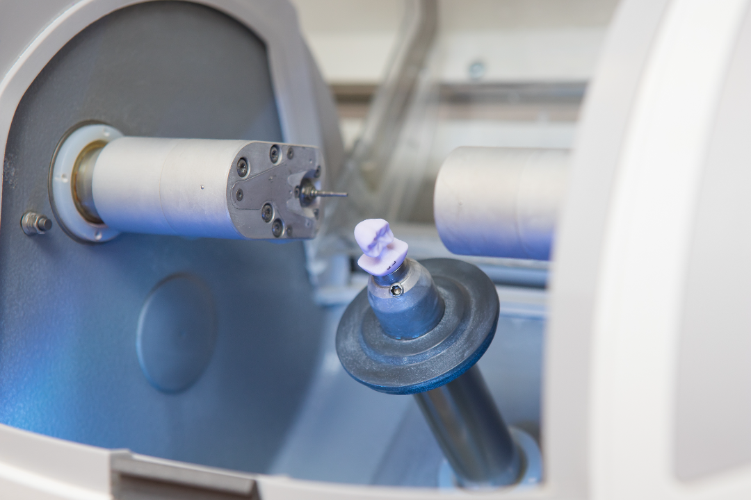 Dental milling machine shaping a dental crown from a purple wax block.