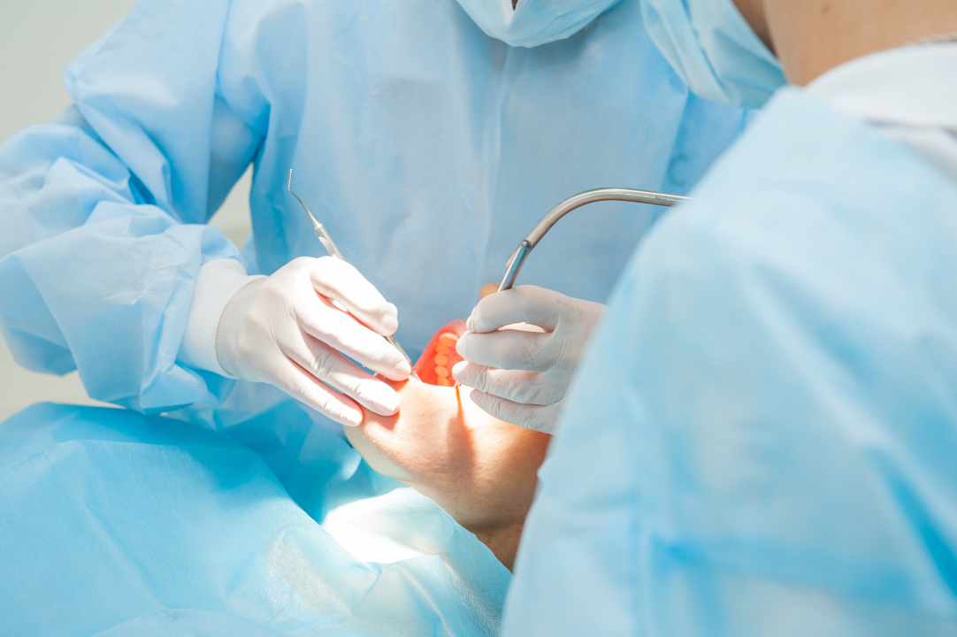 Dentists in blue scrubs and gloves performing a dental procedure on a patient using dental tools.